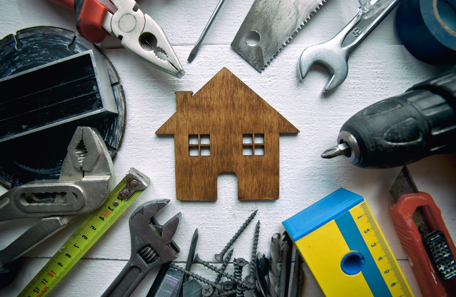 Hand tools laid out around a wooden house model, representing property maintenance for Canberra rentals.